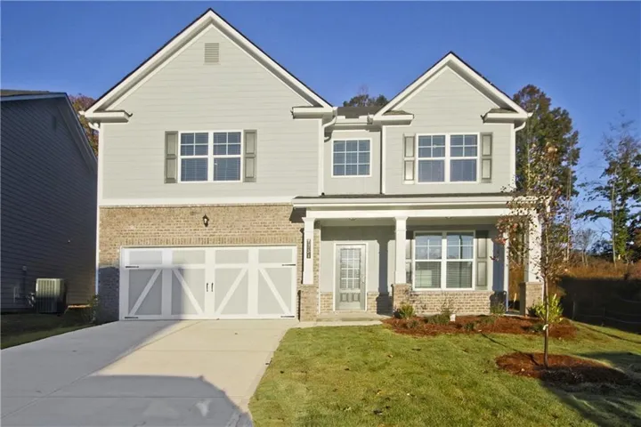 Two-story residence featuring siding and brick facade, an attached two-car garage with decorative doors, a covered front porch, and a concrete driveway