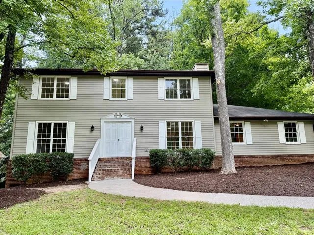 Two-story residence featuring light gray siding with white shutters, a white front entry door with side sconces, and a brick foundation accent