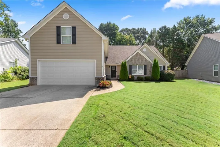 Light-colored siding exterior with brick accents, an attached two-car garage, a concrete driveway, and a front walkway leading to the entry