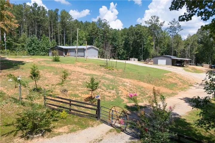 Expansive property featuring a detached garage with an attached carport, a main residence with a covered porch, and a fenced entry