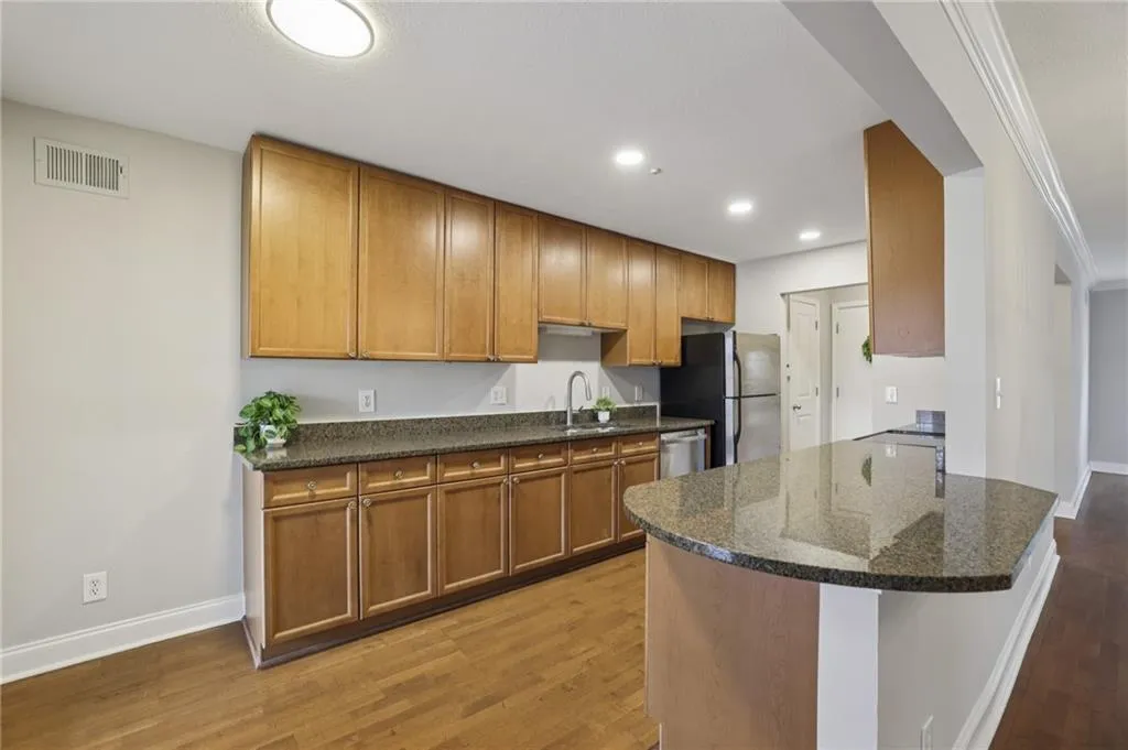Kitchen with light wood finished floors, brown cabinetry, dark stone counters, crown molding, and appliances with stainless steel finishes