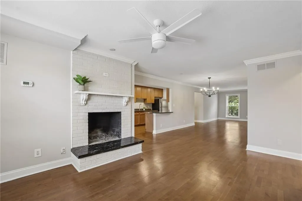 Unfurnished living room featuring a fireplace, ceiling fan, dark wood-type flooring, crown molding, and a chandelier