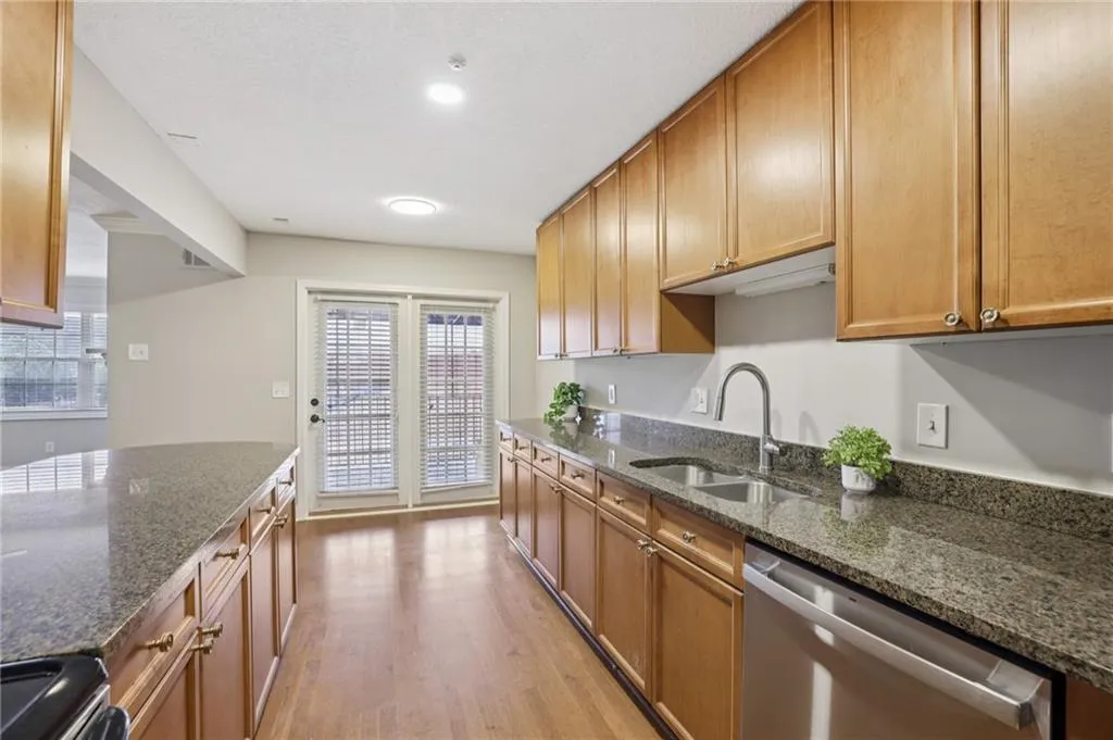 Kitchen with dishwasher, light wood-style floors, dark stone countertops, and range