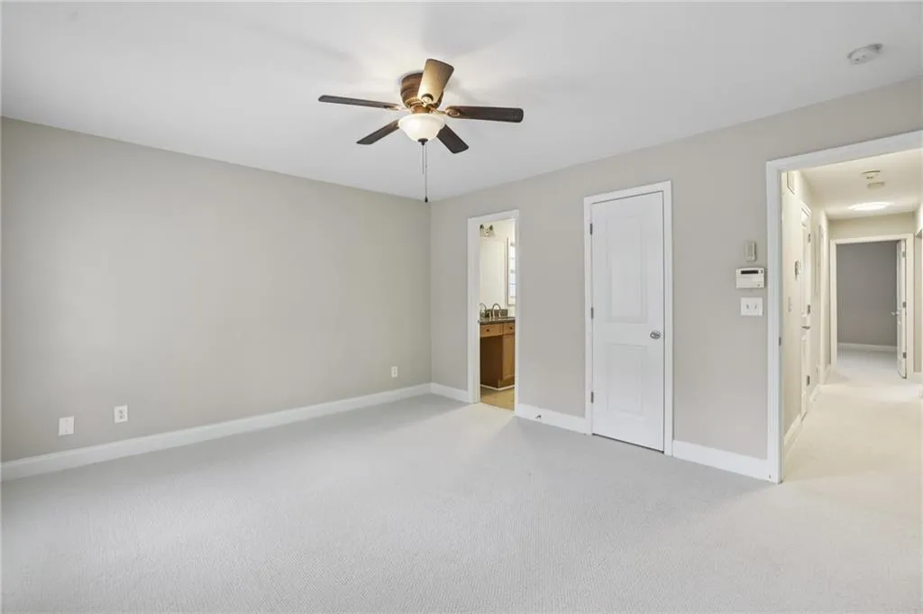 Unfurnished bedroom with light carpet, connected bathroom, and ceiling fan