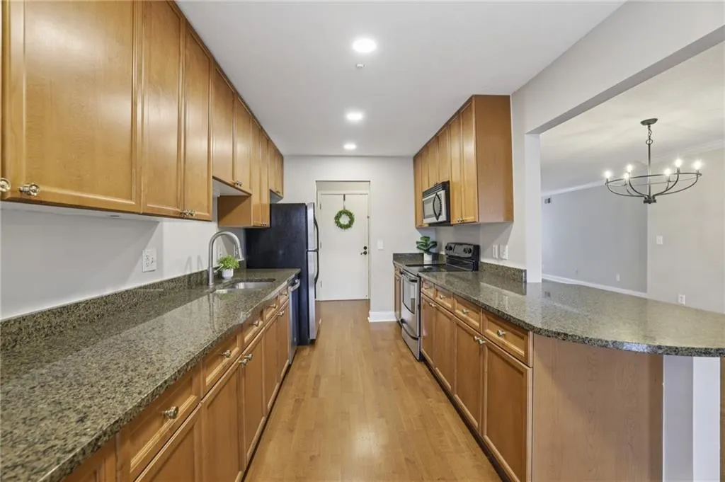 Kitchen featuring stainless steel appliances, light wood-style floors, brown cabinets, dark stone counters, and recessed lighting