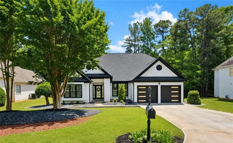 Single-story residence featuring a white facade with black trim, a dark shingle roof, and a two-car garage with modern doors