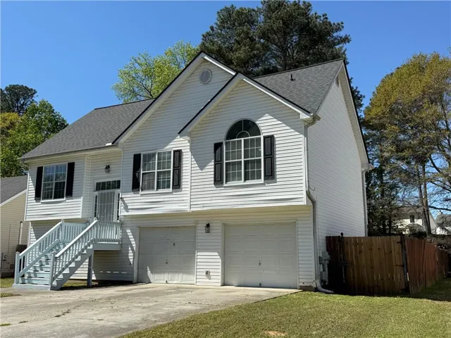 Bi-level home with roof with shingles, driveway, an attached garage, and a gate