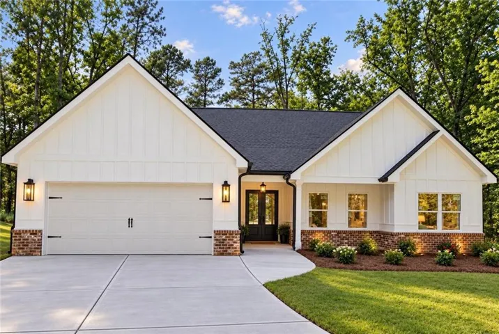 White board and batten siding, shingle roof, brick accent foundation, concrete driveway, and established landscaping