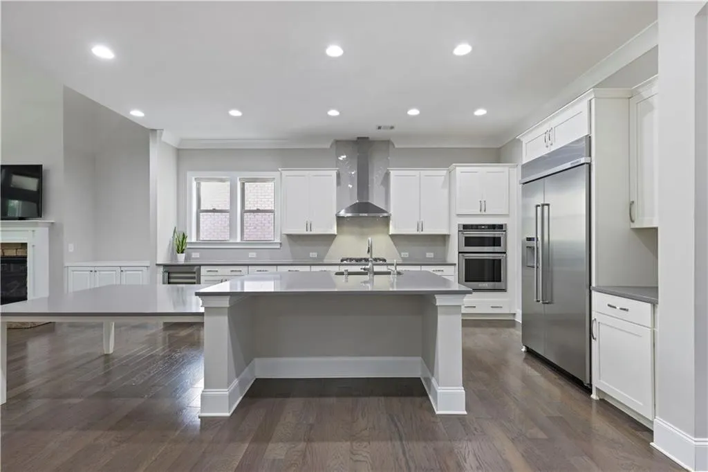 Kitchen with dark wood-type flooring, wall chimney range hood, appliances with stainless steel finishes, and white cabinets