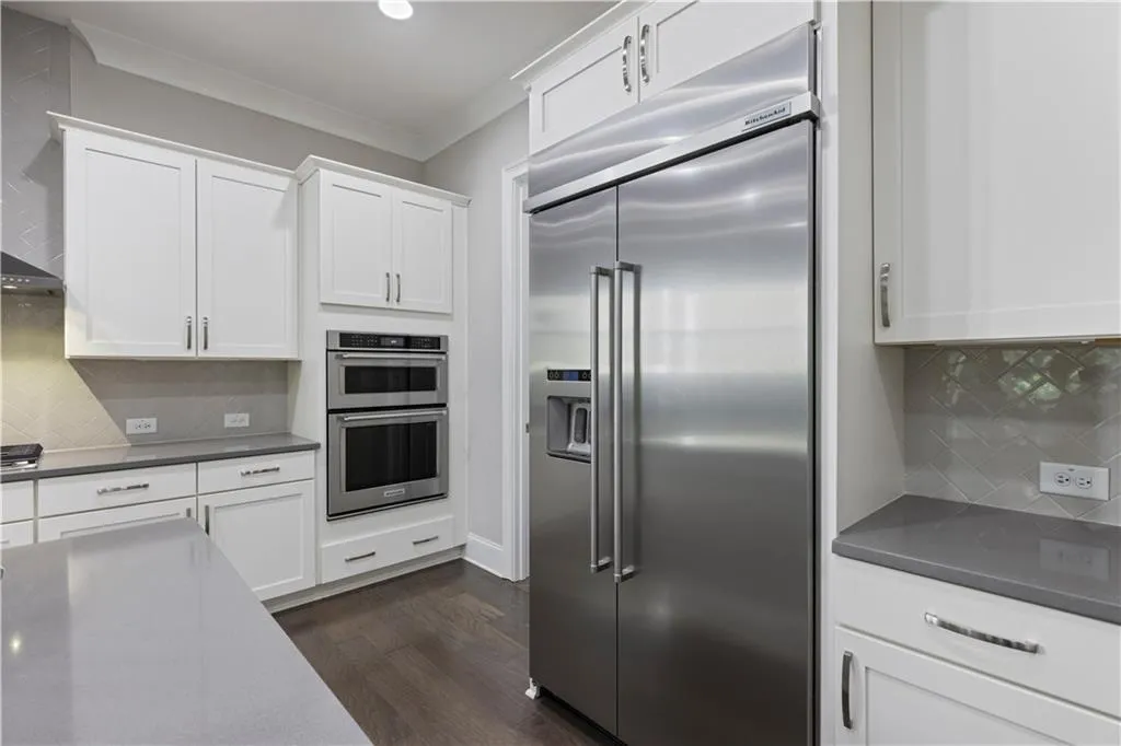Kitchen featuring white cabinets, backsplash, appliances with stainless steel finishes, dark hardwood / wood-style floors, and ornamental molding
