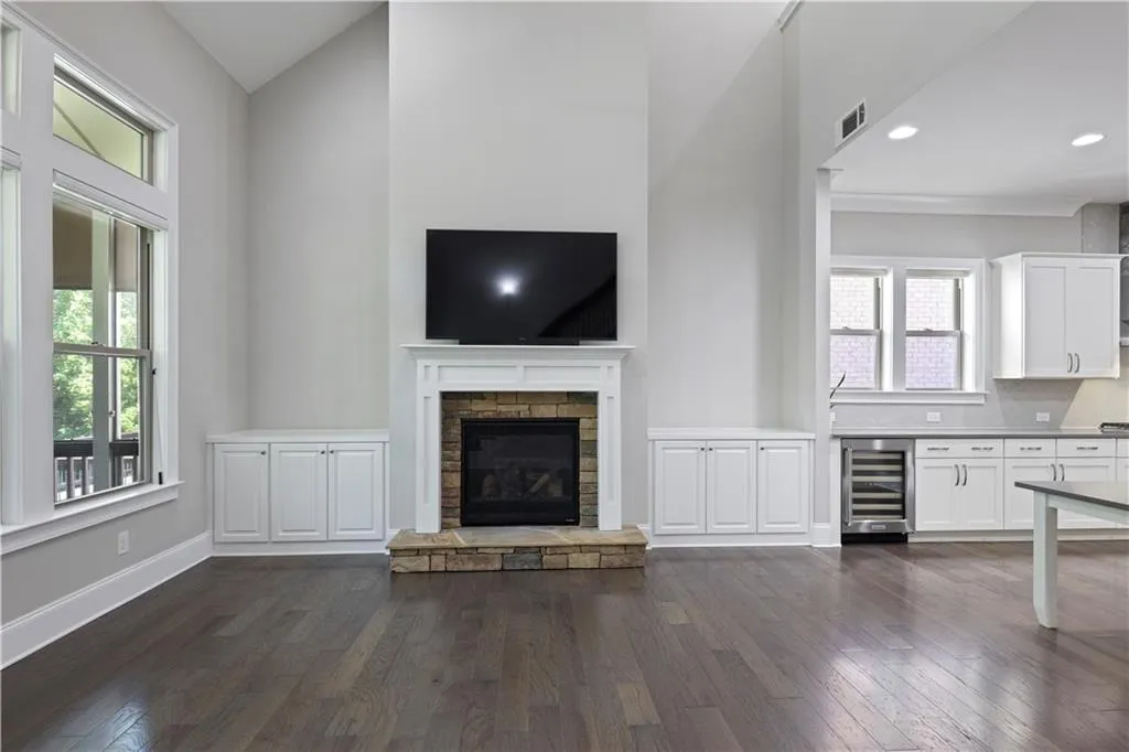 Unfurnished living room with beverage cooler, a stone fireplace, high vaulted ceiling, and dark hardwood / wood-style flooring