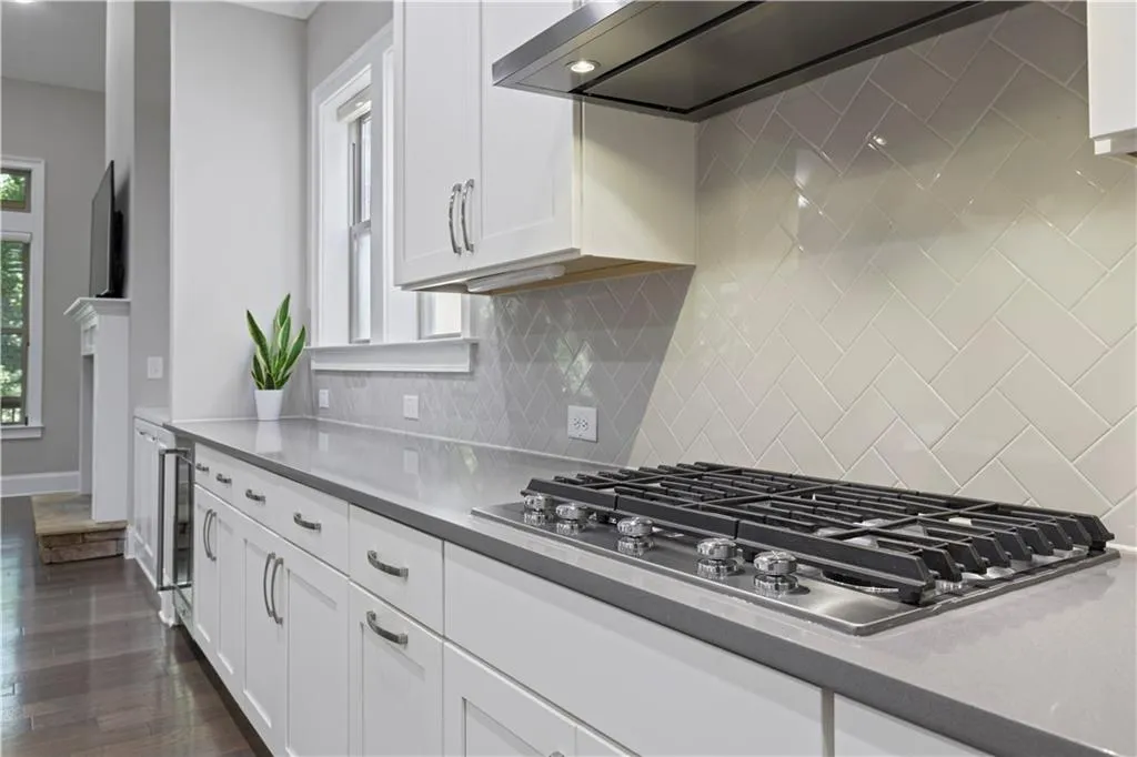 Kitchen with dark wood-type flooring, white cabinets, stainless steel gas stovetop, and wall chimney exhaust hood