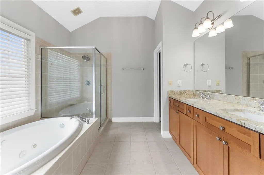 Bathroom with vaulted ceiling, double vanity, a stall shower, light tile patterned flooring, and a whirlpool tub