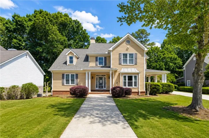 Traditional-style home featuring light yellow siding, dark shutters, a front porch with white columns, a dormer window, and a concrete pathway