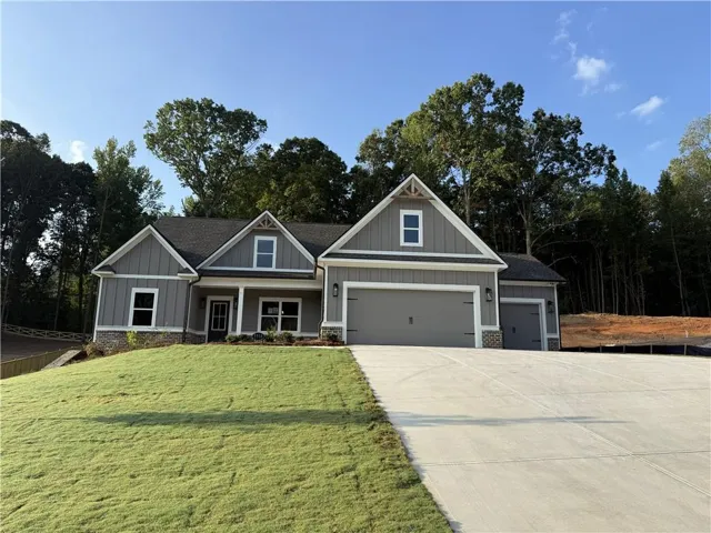 Contemporary exterior with stone accent, dual garage doors, a covered porch, and mature tree landscaping