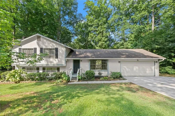 Split-level residence featuring a two-car garage, established landscaping, and mature trees