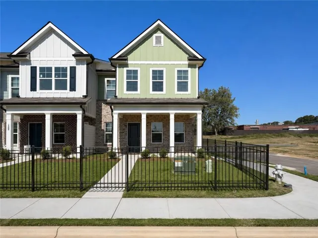Two-story townhome featuring brick and siding exterior, covered front porch with columns, black metal fencing, and manicured front lawn