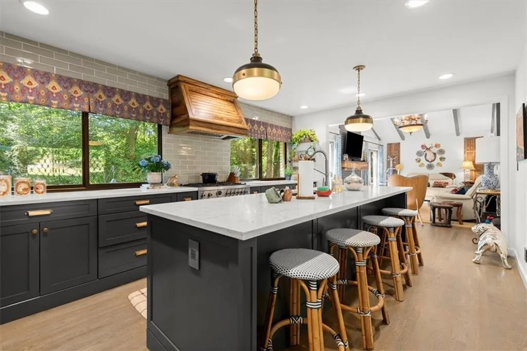 Kitchen featuring light stone countertops, tasteful backsplash, custom exhaust hood, and a kitchen island with sink