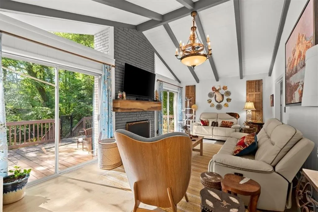 Family room featuring a brick fireplace, vaulted ceiling with beams, an inviting chandelier, and hardwood floors
