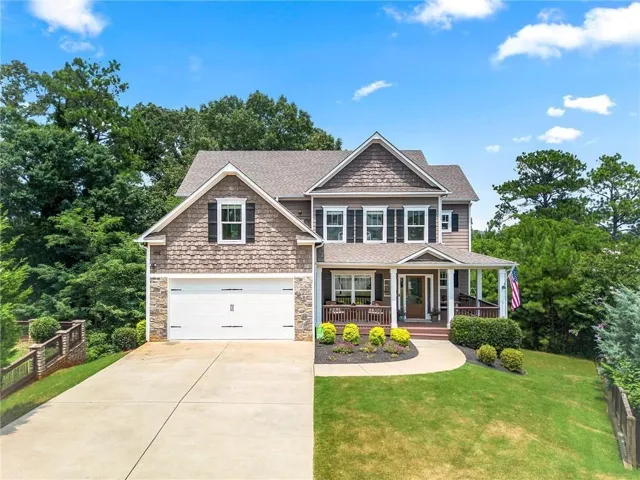 Traditional-style home with a covered front porch, shaker siding, stone accents, attached garage, and a concrete driveway