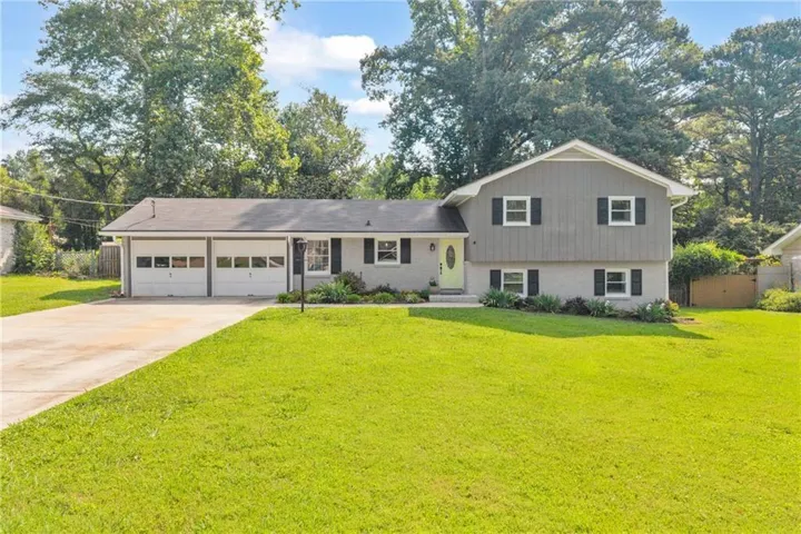 Split-level residence featuring a two-car garage with panel doors, a concrete driveway, and a front lawn