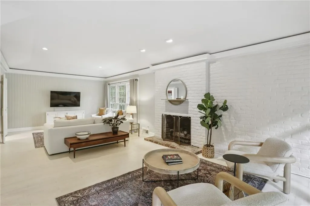 This beautifully designed living room features a functional floor plan that maximizes space. The striking white hardwood floors blend elegantly with the exposed brick surrounding the fireplace, creating a warm and inviting ambiance. Recessed lighting adds a modern touch.