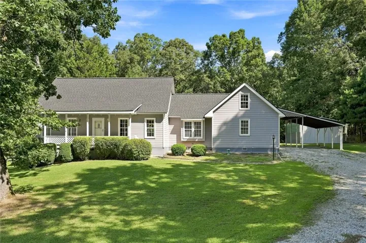 Gabled roofline with asphalt shingles, light gray siding, covered front porch with white railings, and an attached carport