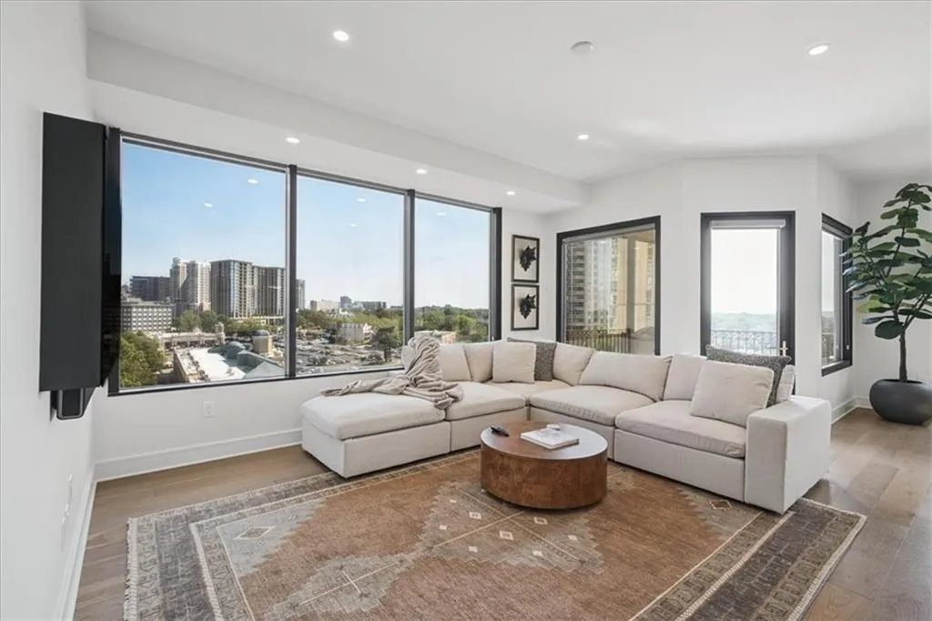 Expansive window wall with urban scenery, recessed ceiling lighting, wood-finish flooring, and white walls