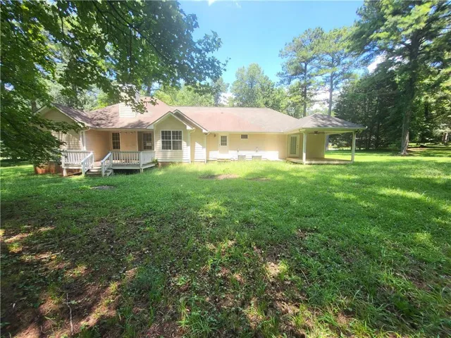Rear exterior featuring a covered porch, an open deck, and mature trees