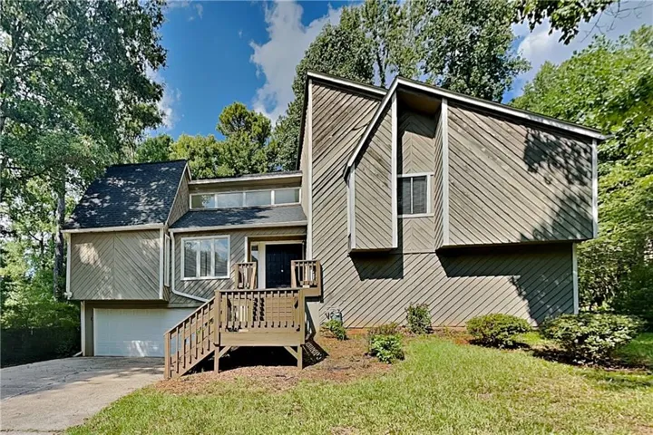 Multi-level exterior with shingled roofing, slatted siding, a multi-pane front window, and an attached garage