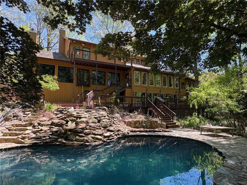 Rear view of property featuring a wooden deck, an outdoor pool, a chimney, and a patio