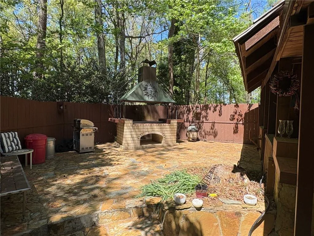 Fenced backyard featuring an outdoor brick fireplace, a gazebo, a patio area, and grilling area