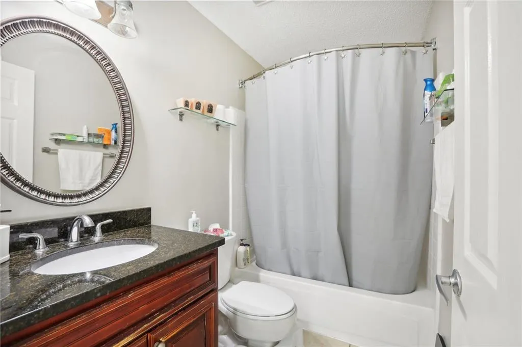 Full bathroom with lofted ceiling, shower / bath combo, vanity, and toilet