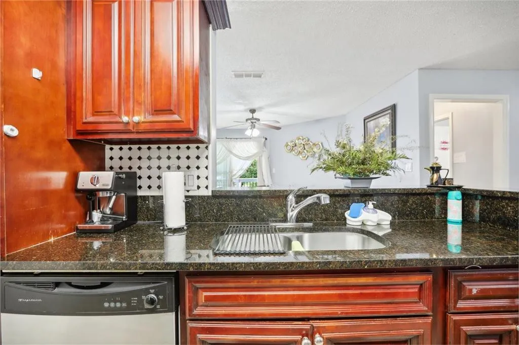 Kitchen with a textured ceiling, dark stone countertops, stainless steel dishwasher, sink, and ceiling fan