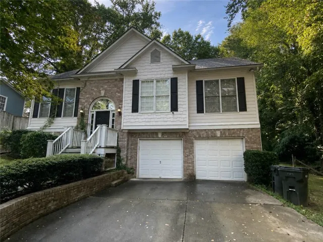 Split-level exterior featuring a two-car garage, brick facade, and white siding