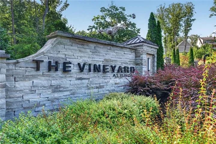 Stone-clad entry monument with metal lettering, featuring integrated landscaping and mature trees