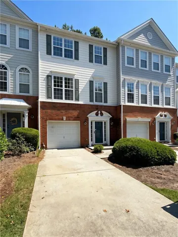 Brick and siding exterior with multiple windows, individual garage, and mature landscaping