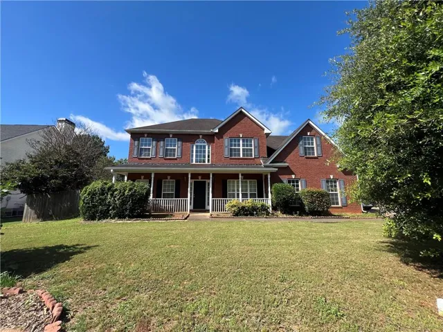 Brick exterior with contrasting shutters, covered front porch with white railings, and a prominent front lawn