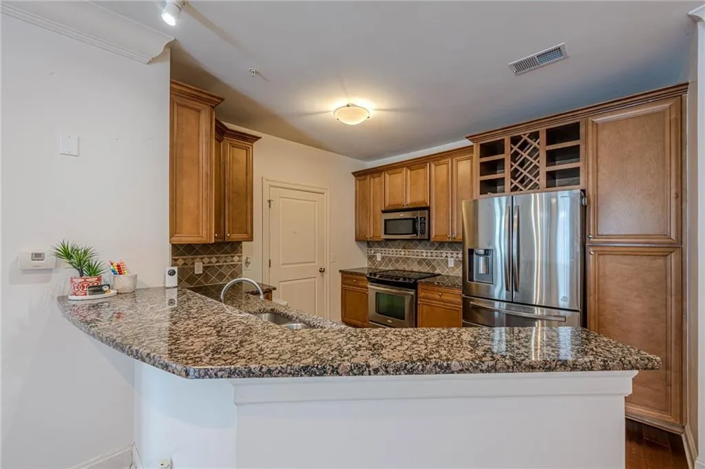 Kitchen with stainless steel appliances, brown cabinets, a peninsula, and backsplash