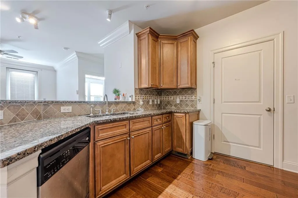 Kitchen with brown cabinets, dishwasher, dark stone countertops, and crown molding
