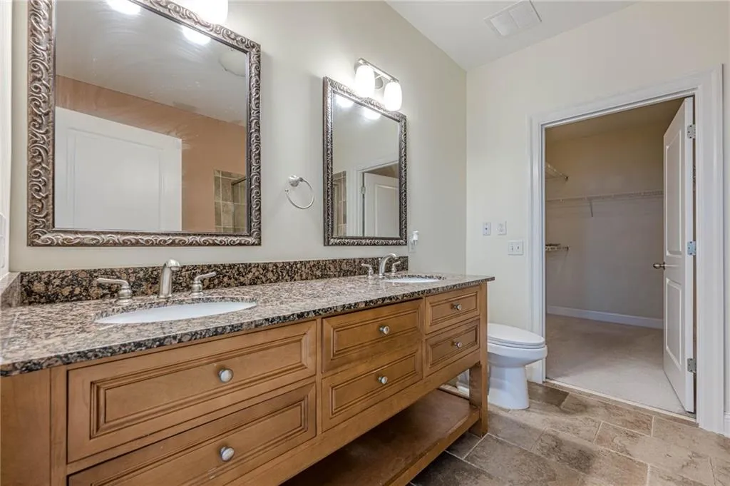 Bathroom with double vanity, a walk in closet, and light stone finish flooring