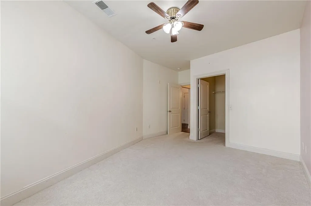 Unfurnished bedroom featuring a walk in closet, light colored carpet, and ceiling fan
