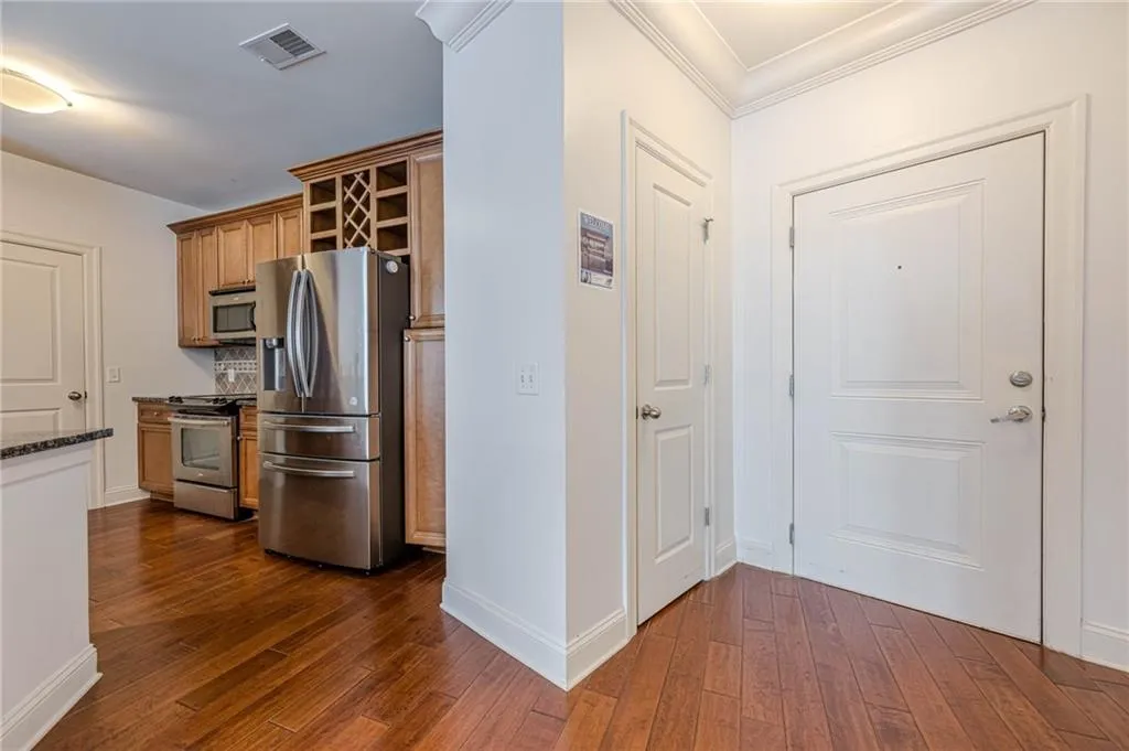 Kitchen featuring appliances with stainless steel finishes, brown cabinetry, dark wood-style flooring, dark stone countertops, and crown molding