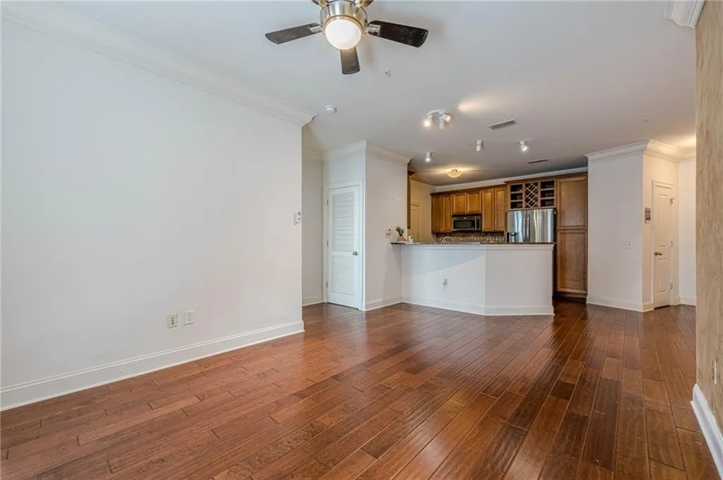Unfurnished living room featuring crown molding, dark wood finished floors, and ceiling fan