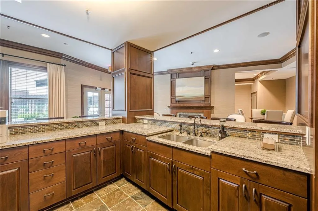 Kitchen with crown molding, backsplash, light stone countertops, brown cabinetry, and recessed lighting