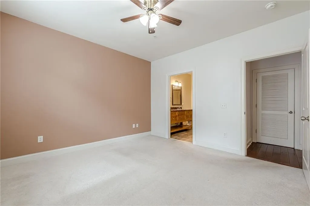 Unfurnished bedroom featuring carpet, a ceiling fan, and ensuite bathroom