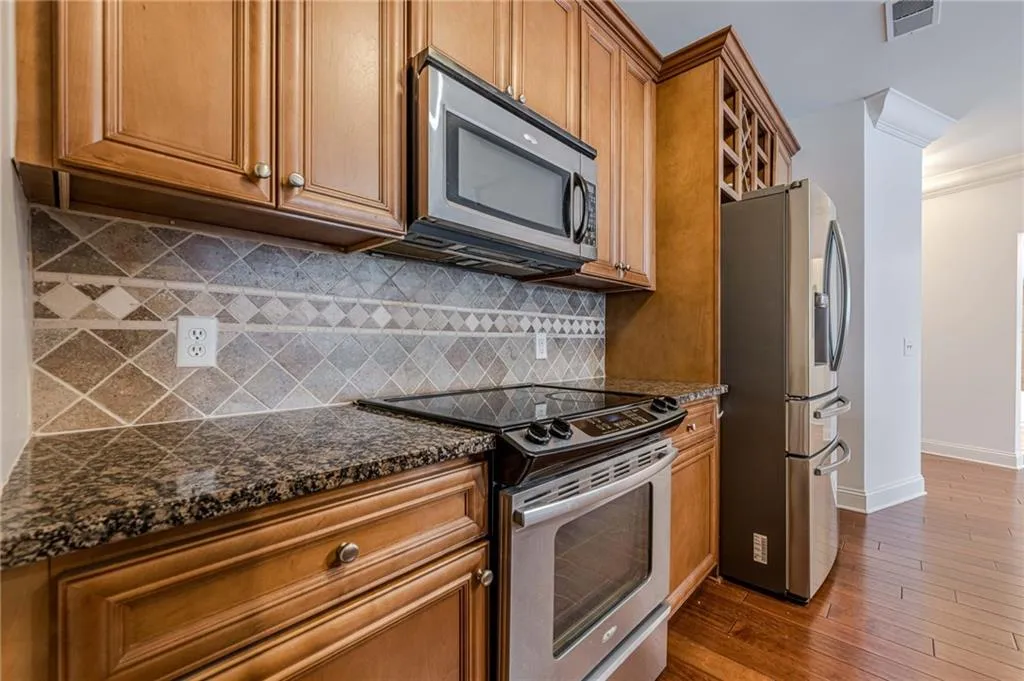 Kitchen with stainless steel appliances, brown cabinetry, dark stone countertops, ornamental molding, and dark wood-style floors