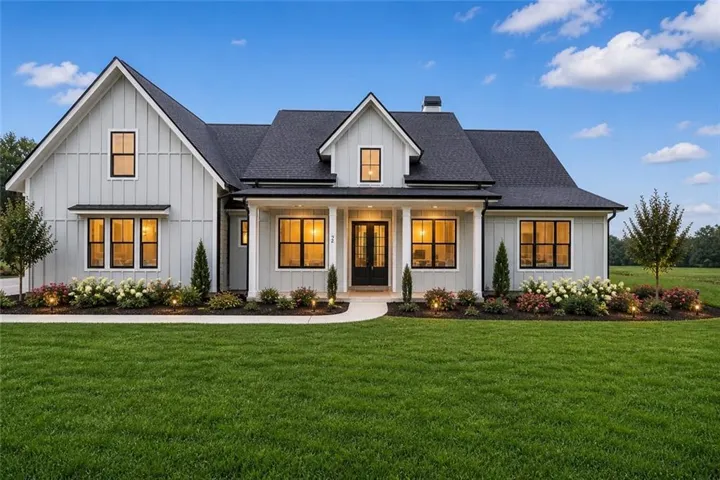 Modern farmhouse exterior featuring light gray board and batten siding, black framed windows, a dark shingle roof, and a covered entry with columns