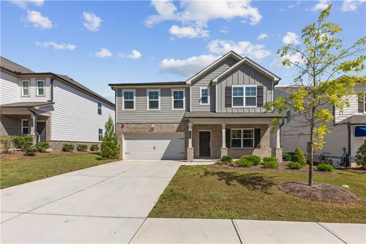 Two-story exterior with a mix of brick and siding, a covered porch with white columns, a two-car garage, and a concrete driveway