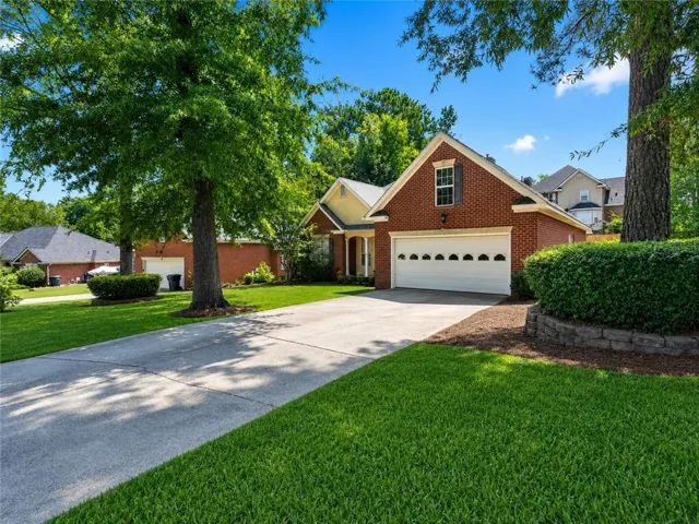 Brick facade residence featuring a two-car garage with decorative windows, a concrete driveway, and mature landscaping